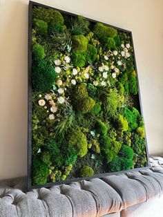 a moss covered wall with white flowers and greenery on the top, in a living room