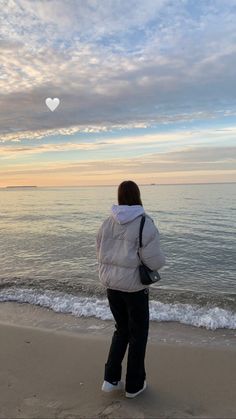 a woman standing on top of a beach next to the ocean under a cloudy sky