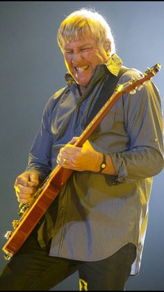 a man with an electric guitar in his hand and mouth wide open, on stage