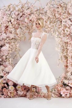 a woman standing in front of a floral backdrop wearing a white dress and high heels