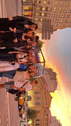 a group of people standing next to each other in front of a tall building at sunset