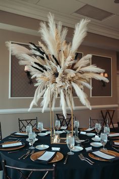 a tall centerpiece with feathers is on top of a round table set for an event