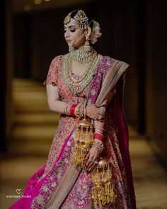 a woman in a pink and gold bridal outfit with jewelry on her head, standing next to stairs