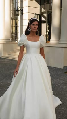 a woman in a white wedding dress is walking down the street with her hand on her hip