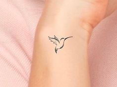 a small black bird tattoo on the left inner arm and wrist, with an outline of a flying bird above it