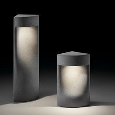 two concrete lamps sitting next to each other on a dark surface with light coming from them