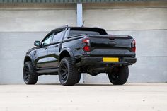 a black truck is parked in front of a concrete wall and has its tail lights on