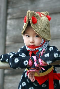 a young child wearing a hat and scarf on top of a wooden fence next to a building