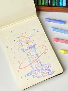 some crayons are next to an open notebook with a drawing on the cover