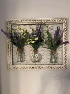 three vases with flowers are hanging on the wall in front of a white frame