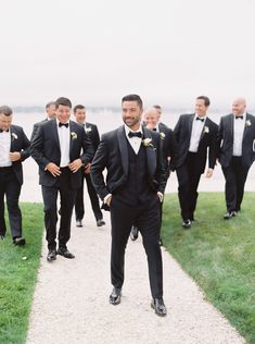 a group of men in tuxedos walking down a path next to the ocean