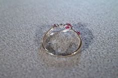 a gold ring with three red stones on it sitting on the floor in front of a gray carpet