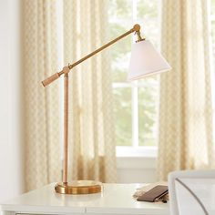 a desk lamp sitting on top of a white table next to a window with curtains