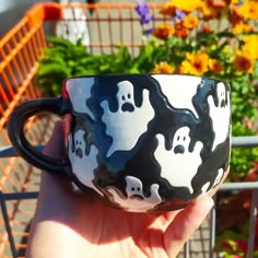 a hand holding a black and white coffee cup with ghost faces on it