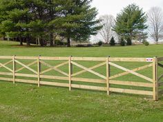 a wooden fence in the middle of a grassy field with trees and grass behind it