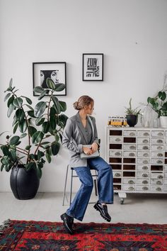 a woman sitting on top of a chair next to a potted plant in a living room