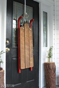 a black door with a red handle and a wooden board hanging from it's side