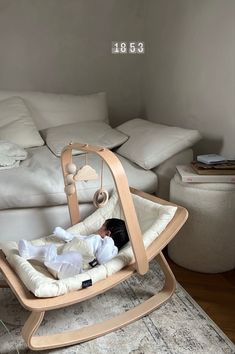 a baby is laying in a wooden cradle on the floor next to a white couch