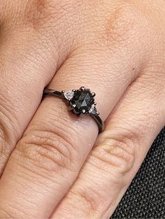 a woman's hand with a black diamond ring on her left hand and the other hand holding an engagement ring