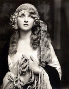 an old black and white photo of a woman with pearls on her head, wearing a scarf