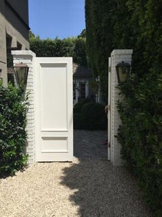 an open door leading to a house with hedges on both sides and a walkway between the two buildings