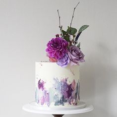 there is a white cake with purple flowers on the top and bottom tiers that are decorated with watercolor paint