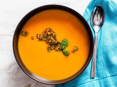 a bowl of carrot soup on top of a blue towel next to a silver spoon