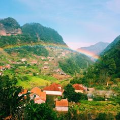 a rainbow in the sky over a small village on a hill with houses and trees