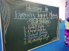 a blackboard with chalk writing on it in front of a blue wall and purple flowers