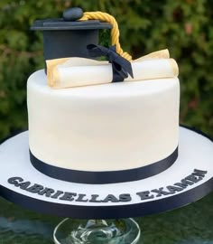 a white cake with black and gold decorations on top is sitting on a glass pedestal