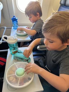 two young boys sitting at a table with food in front of them on an airplane