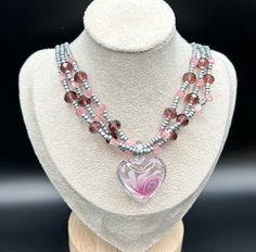 This piece is a graceful, layered heart shaped Andara Crystal necklace and sea bead necklace. The center heart piece has beautiful pink swirls. The colors are absolutely stunning. Colors are light pink to a pleasing purple and grey. This necklace is adjustable. Also, this necklace is lightweight and can be worn all day with ease. Will you add this to your collection? Will not be made again. Pink Heart Beads Pendant Necklace, Pink Beaded Heart Pendant Necklace, Pink Double Strand Necklace For Gift, Pink Heart Pendant Beaded Necklace For Valentine's Day, Pink Necklaces With Heart Charm For Jewelry Making, Pink Beaded Heart Pendant Jewelry, Pink Double Strand Beaded Necklace As Gift, Pink Multi-strand Jewelry Gift, Pink Beaded Necklace With Heart Pendant As Gift