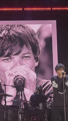 two men on stage with microphones in front of a large poster