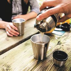 two people sitting at a table with cups and one person pouring something into the cup