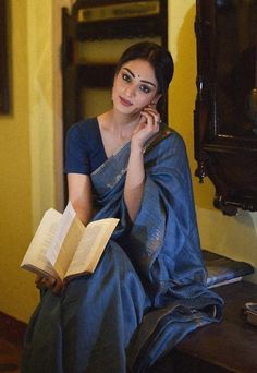 a woman sitting on a chair while talking on a cell phone and holding an open book