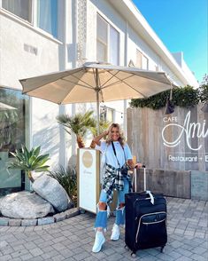 a woman is posing with her luggage under an umbrella