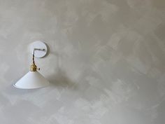 a white wall mounted light on the side of a gray wall with a gold hook