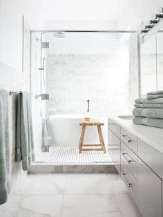 a bathroom with white marble walls and floor, along with a wooden stool in front of the bathtub