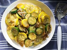 a white bowl filled with zucchini and other vegetables on top of a blue towel