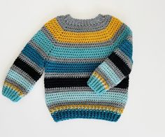 a crocheted sweater is shown on a white surface with a blue, yellow and black stripe