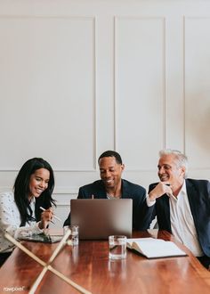 three people sitting at a table looking at a laptop computer and smiling for the camera