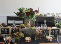 a table topped with wine bottles and desserts next to a vase filled with flowers