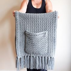 a woman is holding up a crocheted blanket