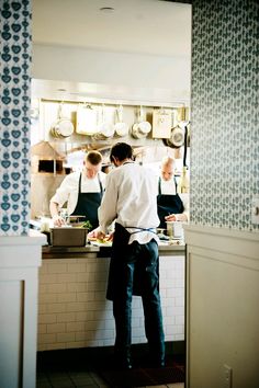 two men in aprons are preparing food in a kitchen with blue and white wallpaper