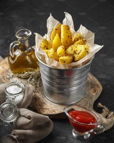 a metal bucket filled with bananas next to some ketchup on a wooden tray