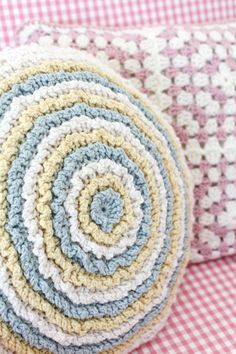 a crocheted round pillow sitting on top of a pink and white checkered blanket