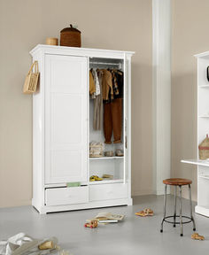 a white armoire with clothes hanging on it and stools in front of it