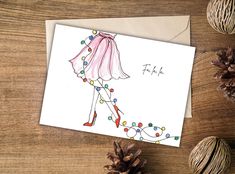 a card with a drawing of a woman's dress and shoes on it, next to pine cones