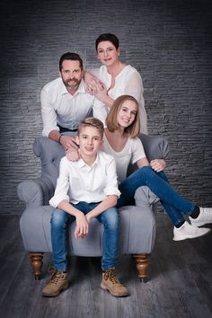 a family sitting on a grey couch posing for a photo in front of a brick wall