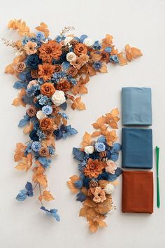 an arrangement of blue and orange flowers on a white surface next to a pair of scissors